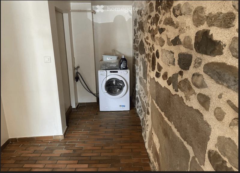 Hallway with a washing machine, tiled floor, and stone wall.