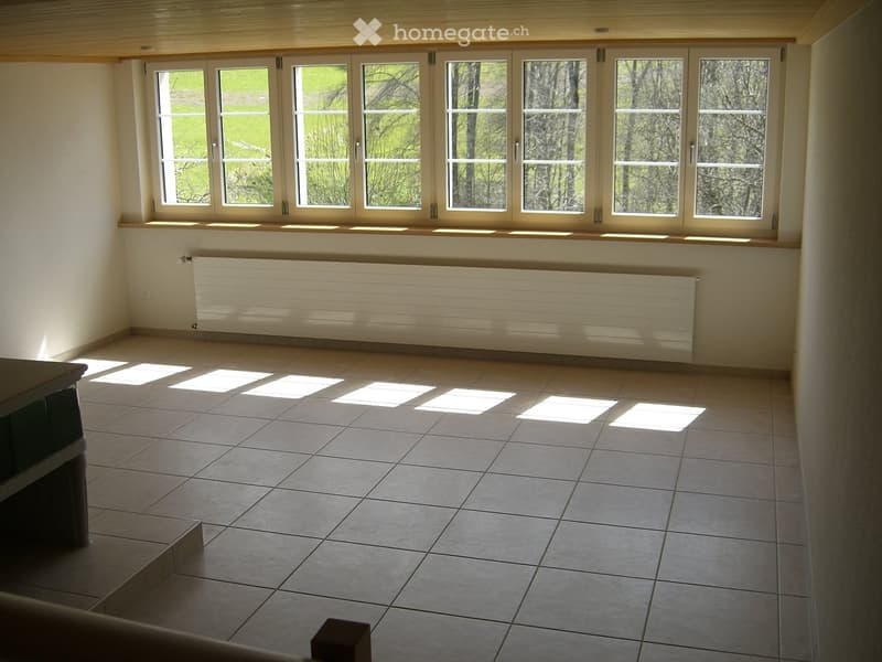 Empty room with tiled floor, large windows, radiator, and wooden ceiling beams.