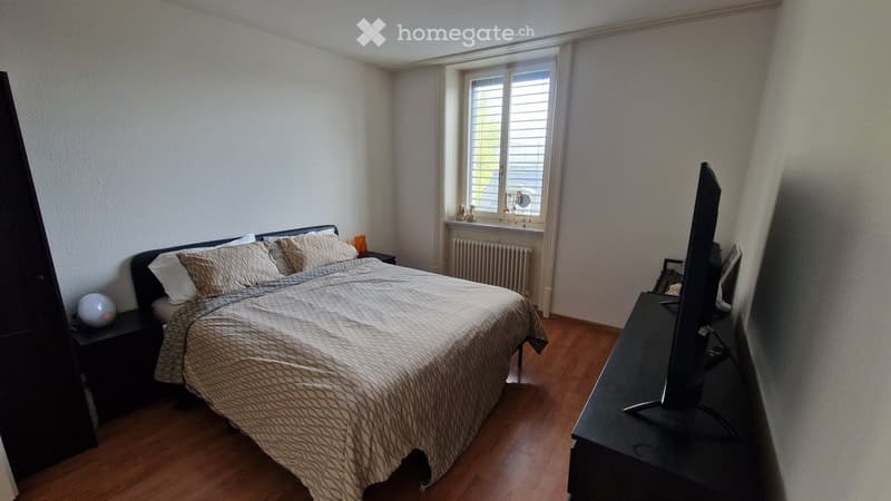 Bedroom with a large bed, nightstand, television, and a decorative ball on the nightstand. The room has wooden flooring and large windows with blinds.