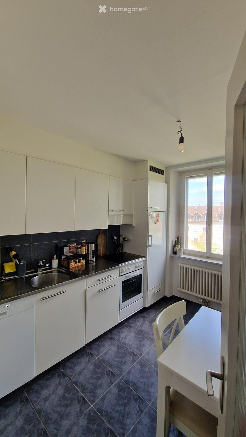 Modern kitchen with white cabinets, stainless steel appliances, dark tiled floor, and a small dining area with a table and chair.