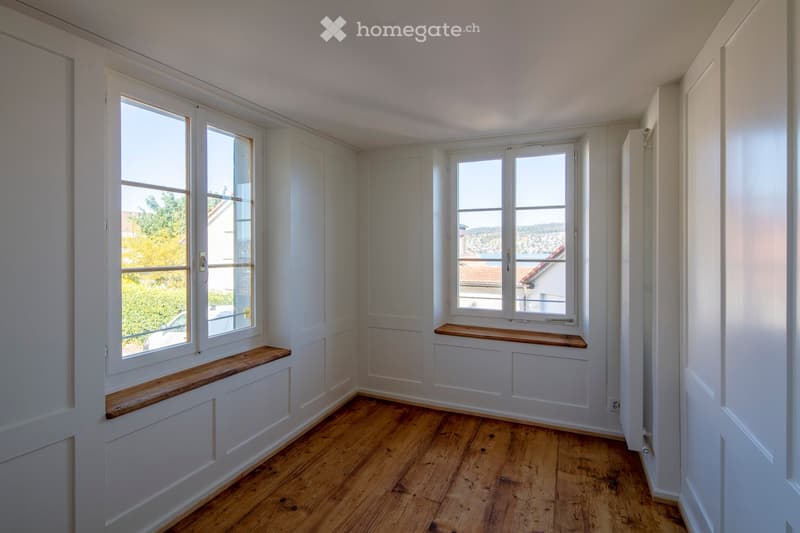 Empty room with wooden flooring, white walls, and large windows with wooden sills. No furniture or equipment present.