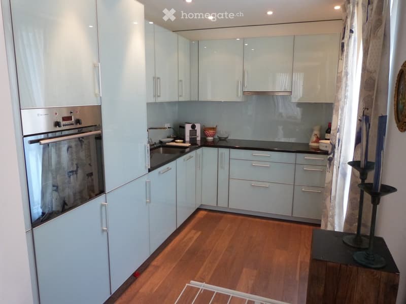 Modern kitchen with white cabinets, stainless steel appliances, and a wooden floor.