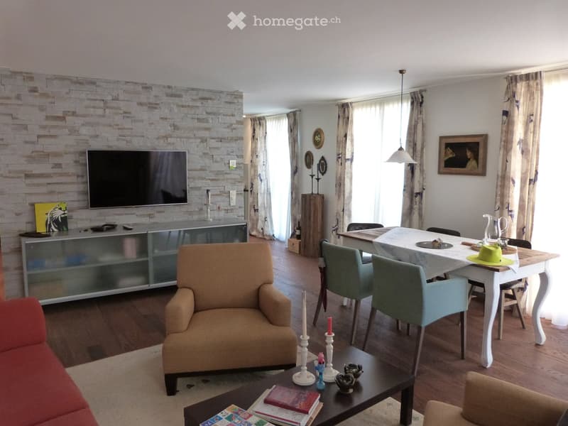 Open living room with dining area, TV, carpet, wooden floors, dining table with chairs, armchair, center table, sideboard, picture frames, curtains, and windows