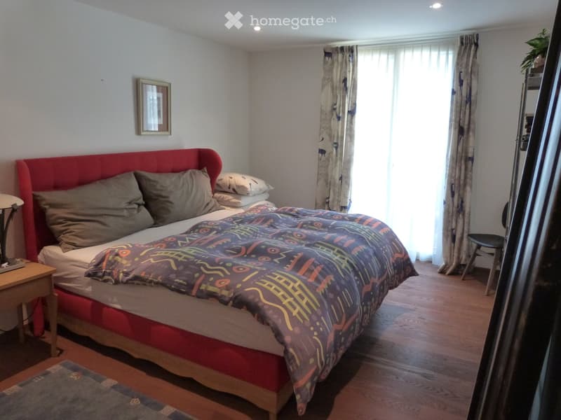 large double bed with bedspread, wall frame, wooden floor, lamp, chair, curtain
