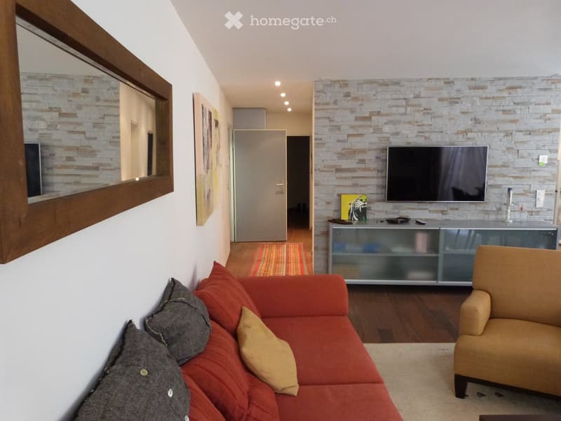 Modern living room with orange couch, brown armchair, tiled wall, flatscreen TV, wooden floor