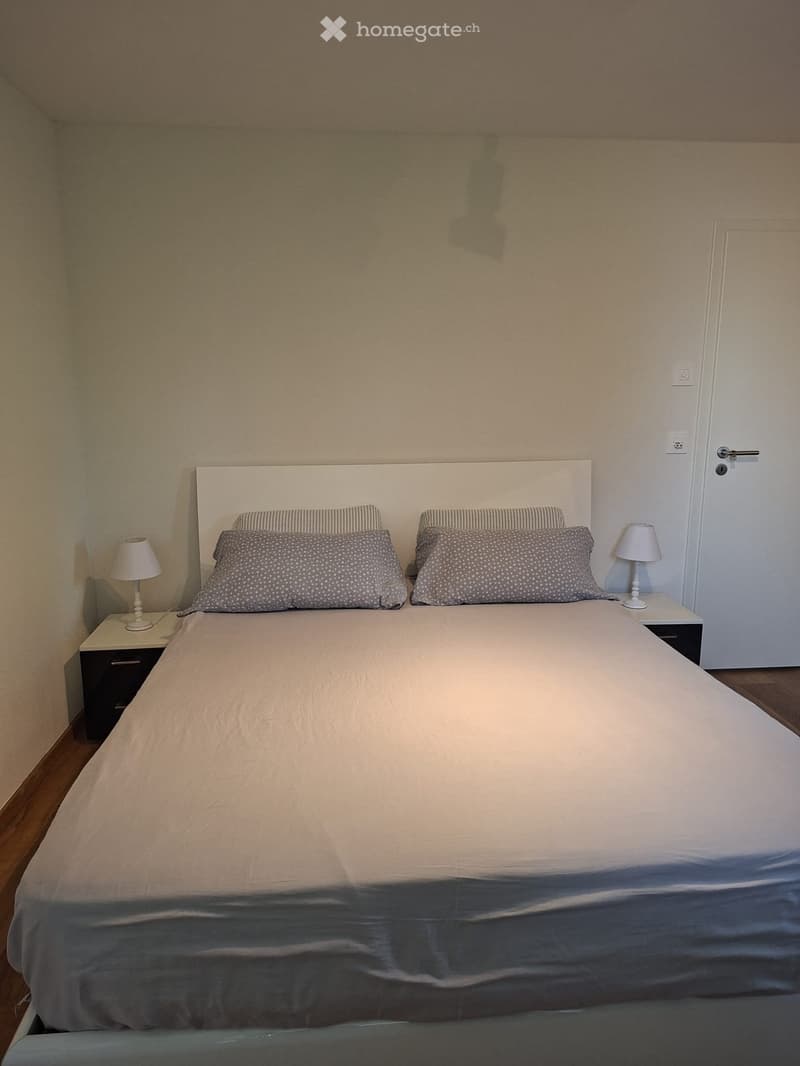 A neatly made double bed with a white headboard, two nightstands with lamps, and matching pillows.