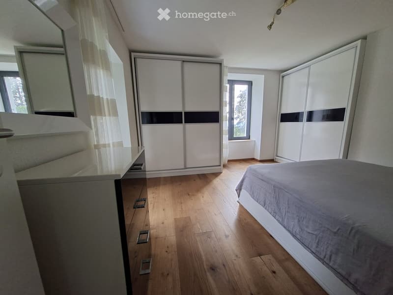 Modern bedroom with wooden flooring, large bed, mirrored wardrobe, and large windows with sheer curtains.