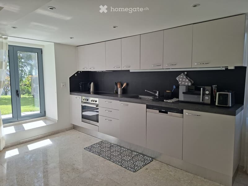 Modern kitchen with white cabinets, stainless steel appliances, and a black countertop. Features an oven, dishwasher, microwave, and various kitchen utensils.