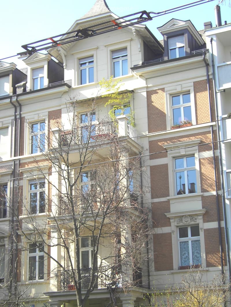 Multi-story residential building with brick and white facade, multiple windows, balconies, and decorative architectural details.