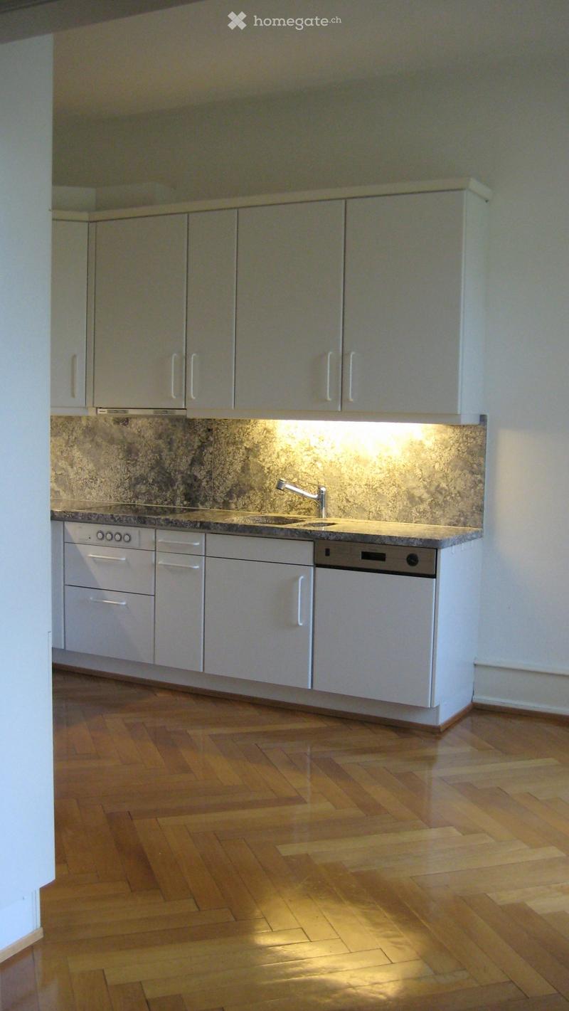 Modern kitchen with white cabinets, granite countertop, and wooden flooring.