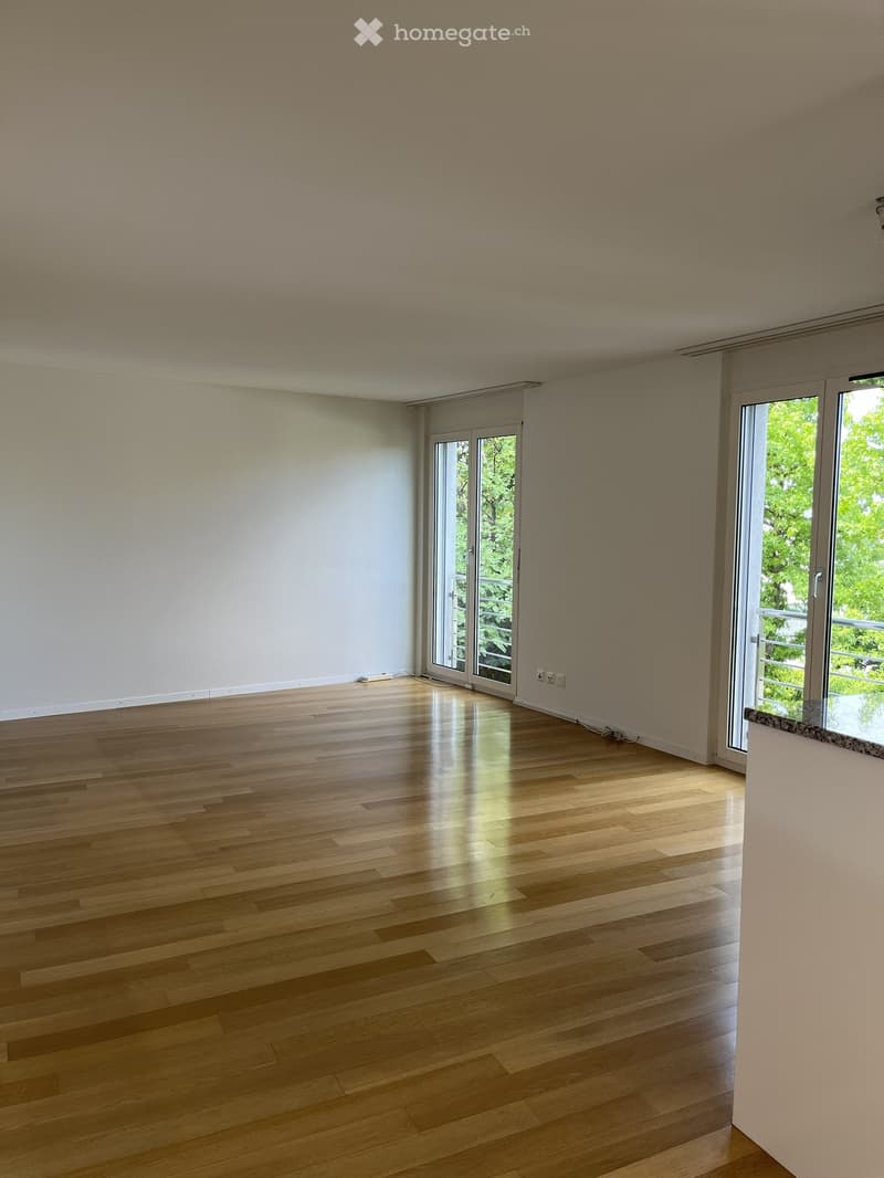 Empty room with wooden flooring, white walls, and large glass doors leading to a balcony or outdoor area.
