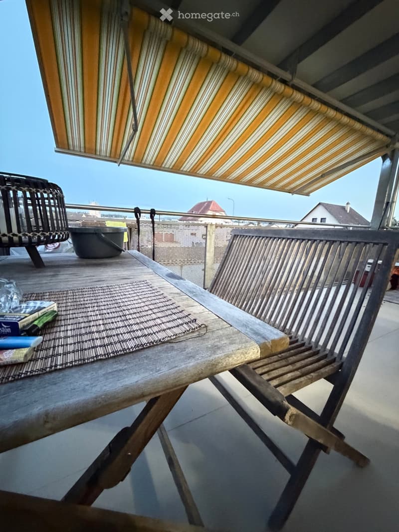 Balcony with wooden table, wicker chair, and a view of the surrounding area.