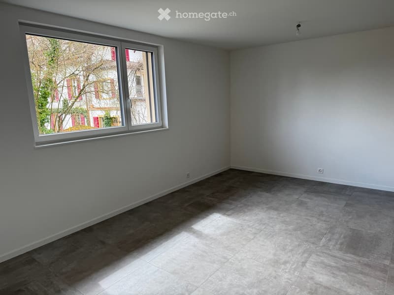 Empty room with light grey walls, large window, and tiled floor. No furniture or equipment visible.