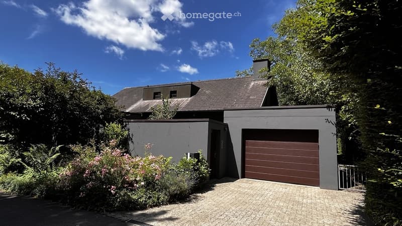 Modern two-story house with grey exterior, dark brown garage door, and surrounding greenery.