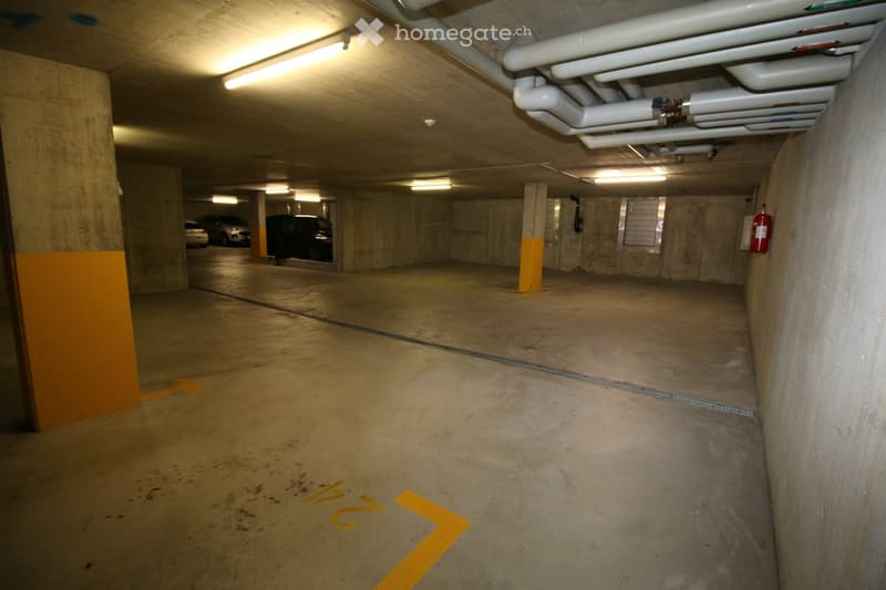 Underground parking area with concrete pillars, parked cars, and overhead lighting.