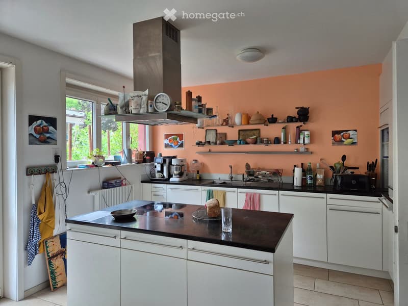 Modern kitchen with white cabinets, black countertops, and a central island. Features include a sink, faucet, oven, coffee maker, toaster, microwave, and various kitchen utensils and appliances on shelves and countertops.