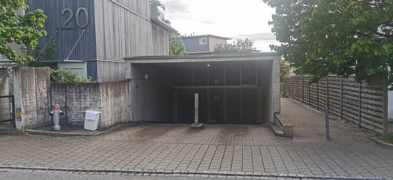 Building. Modern building entrance with a covered garage area, brick pavement, and a concrete wall on one side.