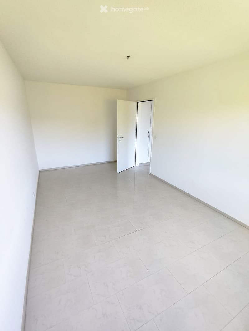 Empty room with light-colored tiled flooring and white walls, featuring an open doorway leading to another space.