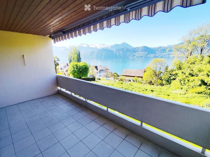 Balcony with tiled floor, wooden ceiling, striped awning, overlooking a lake and mountains.