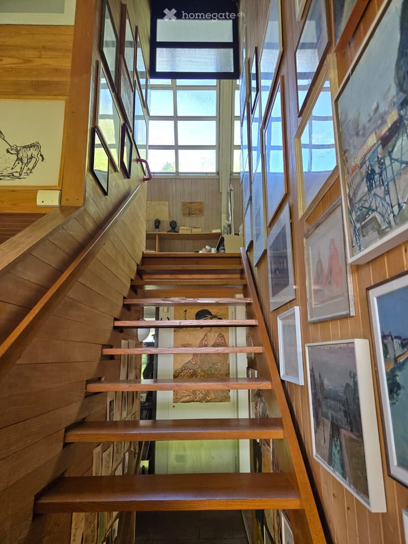 Corridor / Hallway. Wooden staircase with handrails, large windows, and framed artwork on the walls.