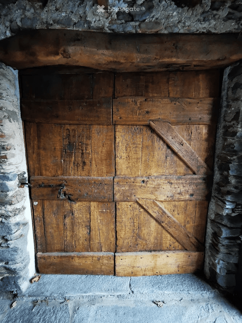 A rustic wooden door set within a stone wall, featuring a traditional design with visible wear and natural wood grain.