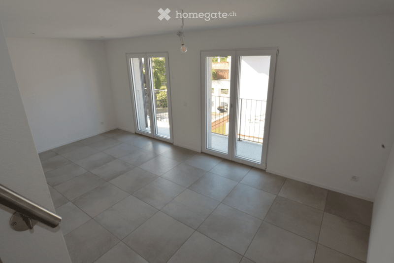 Empty room with tiled floor, white walls, and two sliding glass doors leading to a balcony.