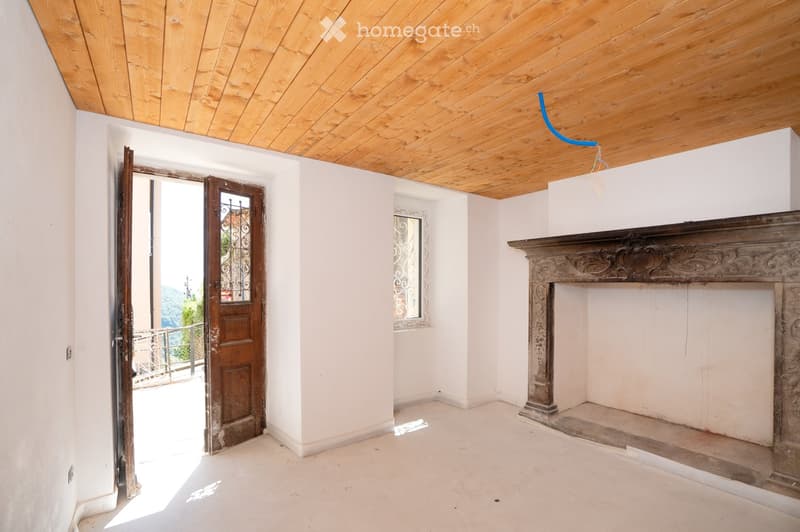 Empty room with white walls, wooden ceiling, fireplace, and open door leading to a balcony.