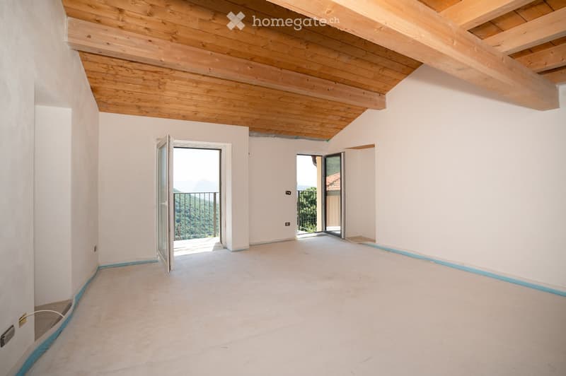 Empty room with white walls, wooden ceiling, and two open doors leading to a balcony with a scenic view.