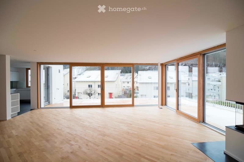 Bright, empty room with wooden flooring and large sliding glass doors leading to a balcony or outdoor area. The walls are painted in a light neutral color, and the space is well-lit with natural light.