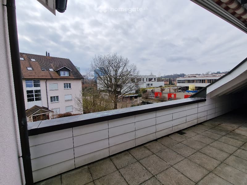 Balcony with tiled floor and white wooden railing, overlooking a residential area with houses and trees.