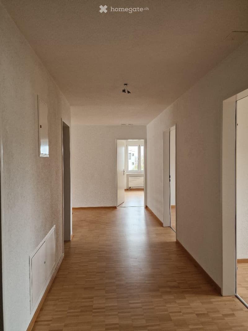 Empty hallway with wooden flooring, white walls, and several open doors leading to other rooms.
