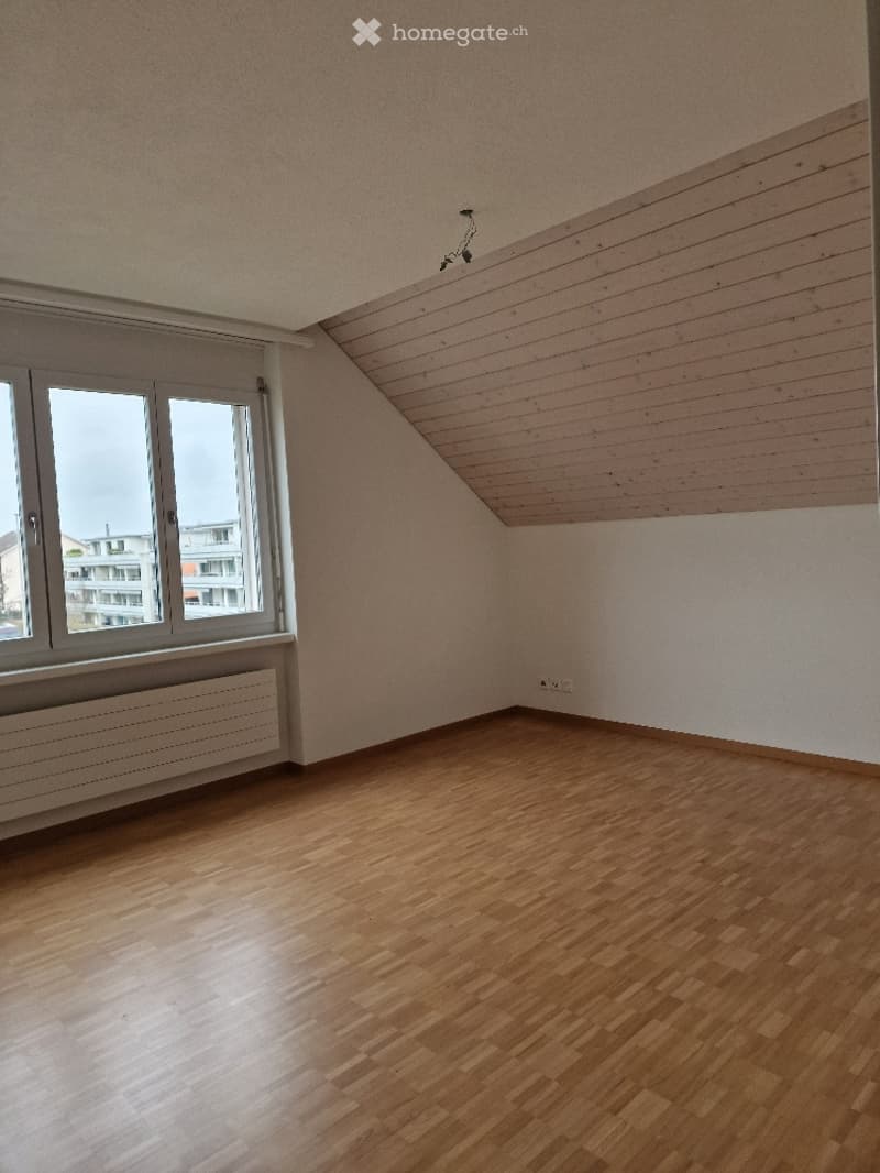 Empty room with wooden flooring, white walls, large window, and radiator. No furniture or equipment present.