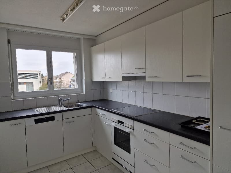 Modern kitchen with white cabinets, black countertops, and stainless steel appliances including a sink, oven, and dishwasher. Large window provides natural light.