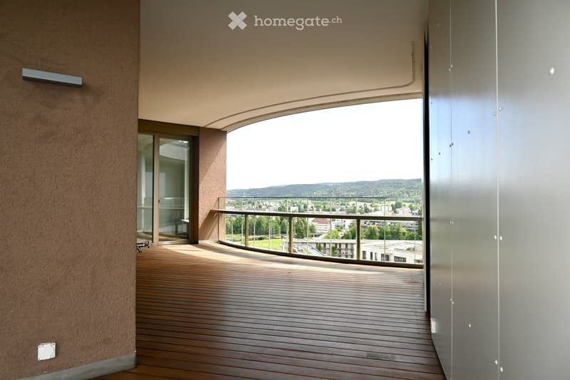 Modern balcony with wooden decking, glass railing, and scenic view of the city and surrounding landscape.