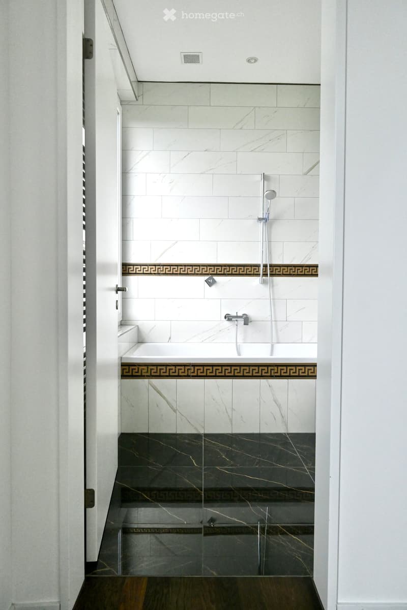 Modern bathroom with a bathtub, marble tiles, and a glass shower enclosure. Features a decorative border and sleek fixtures.