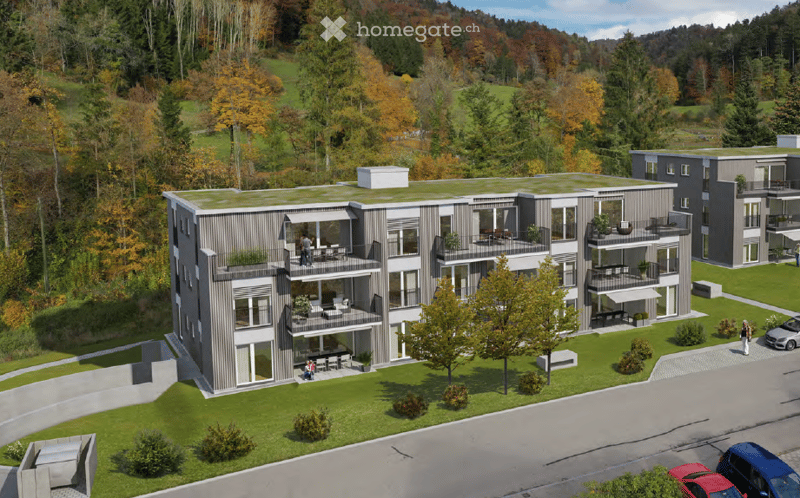Modern multi-story residential building with balconies, surrounded by green lawn and trees, with several parked cars nearby.