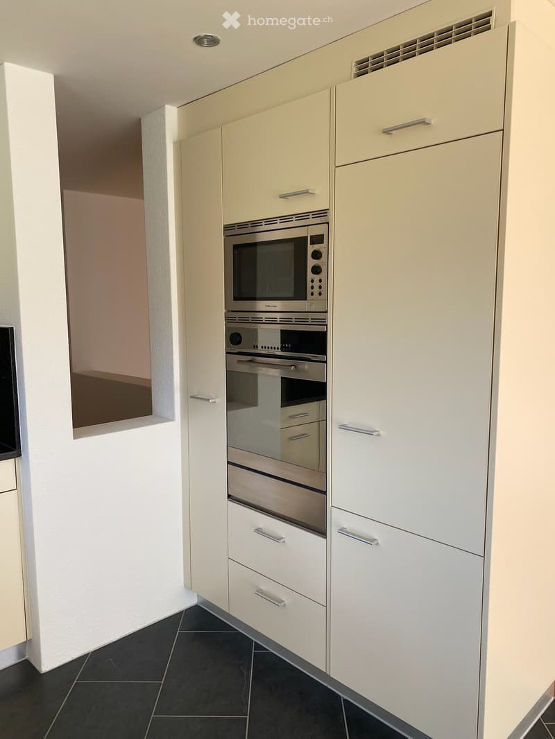 Modern kitchen with white cabinets, stainless steel microwave and oven, dark tiled floor, and sleek design.