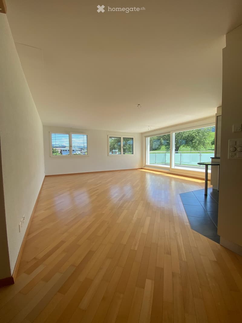 Empty room with wooden flooring, large windows, and a small table near the balcony entrance.