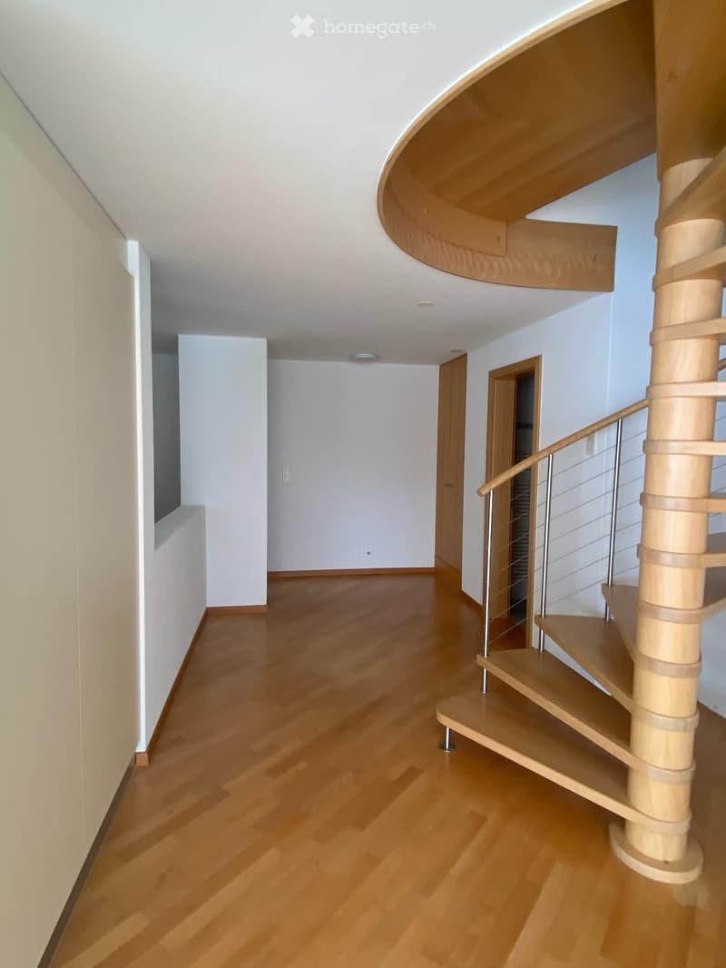 Spacious hallway with polished wooden flooring, white walls, and a modern spiral staircase with wooden steps and metal railing.