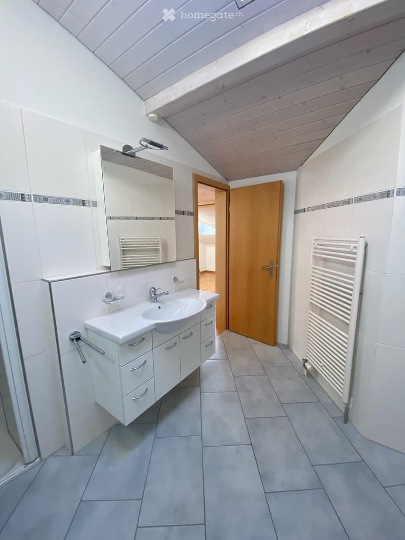 Modern bathroom with white tiled walls, a white sink with a mirror, a radiator, and a wooden door leading to another room.