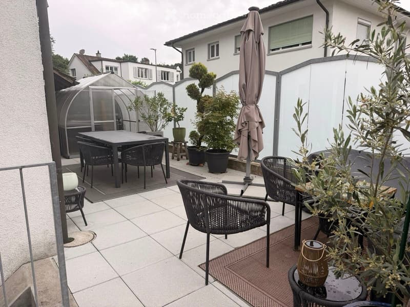 Outdoor patio with tiled flooring, several potted plants, a dining table with chairs, and a lounge area with additional chairs and a small table.