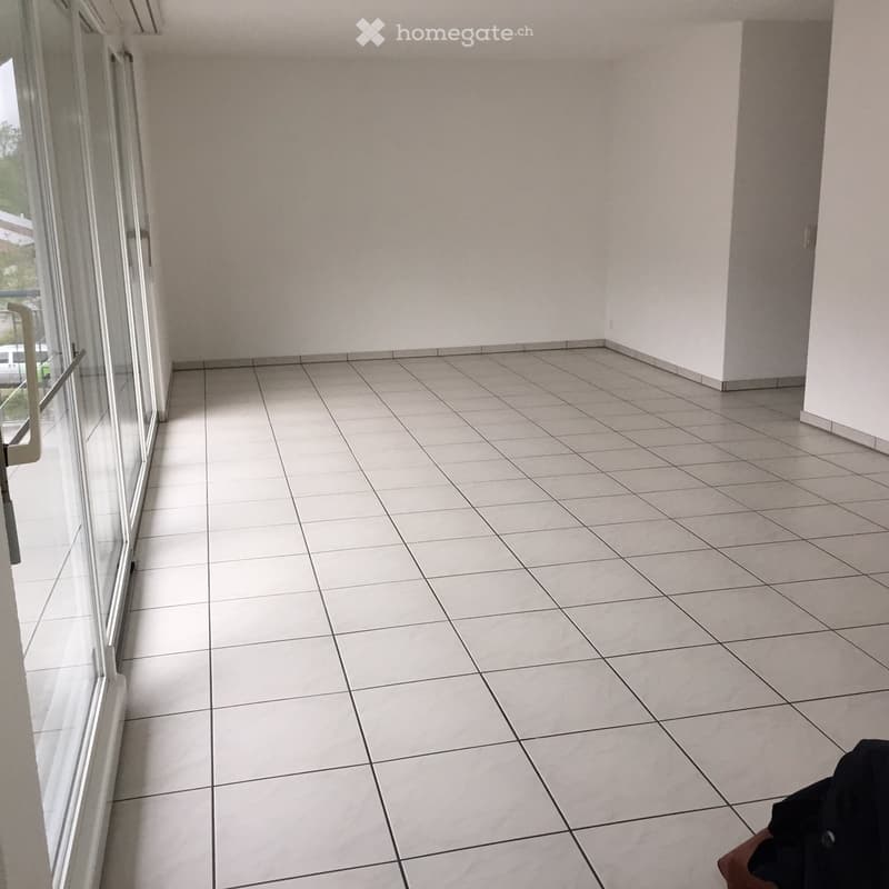 Empty balcony with tiled floor and large glass door leading to the interior.