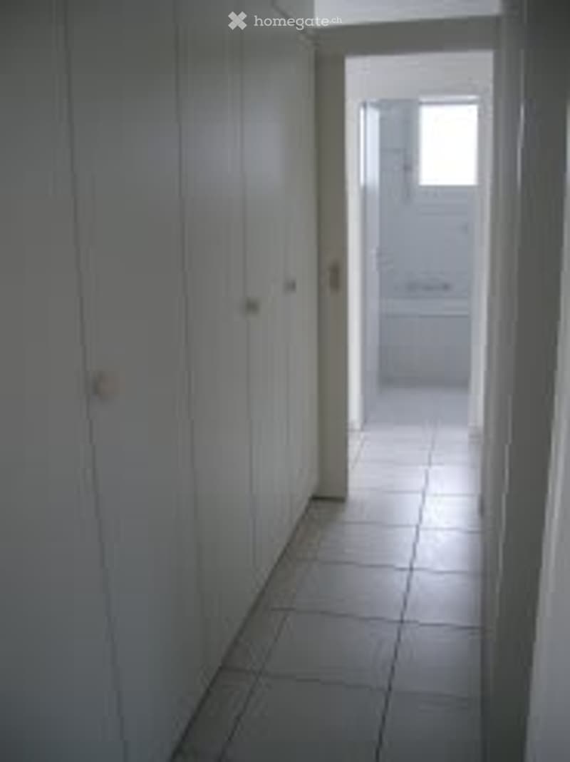 Corridor with tiled flooring and white cabinets.