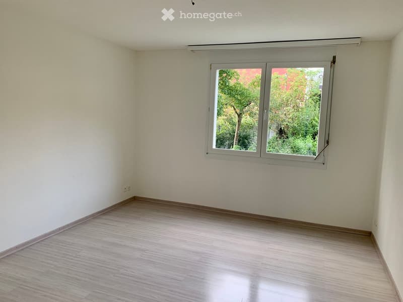 Empty room, white walls, wooden floor, window with garden view.