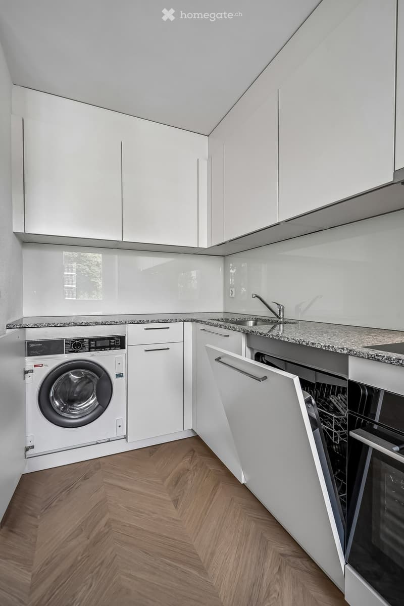 Modern kitchen with white cabinets, granite countertop, wooden herringbone floor, integrated washing machine and dishwasher.