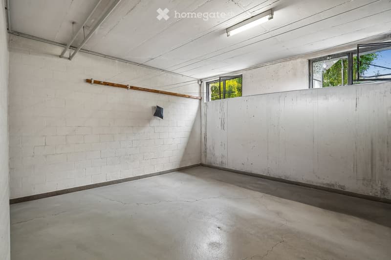 Empty room with white brick walls, concrete floor, and large windows allowing natural light. No furniture or equipment present.