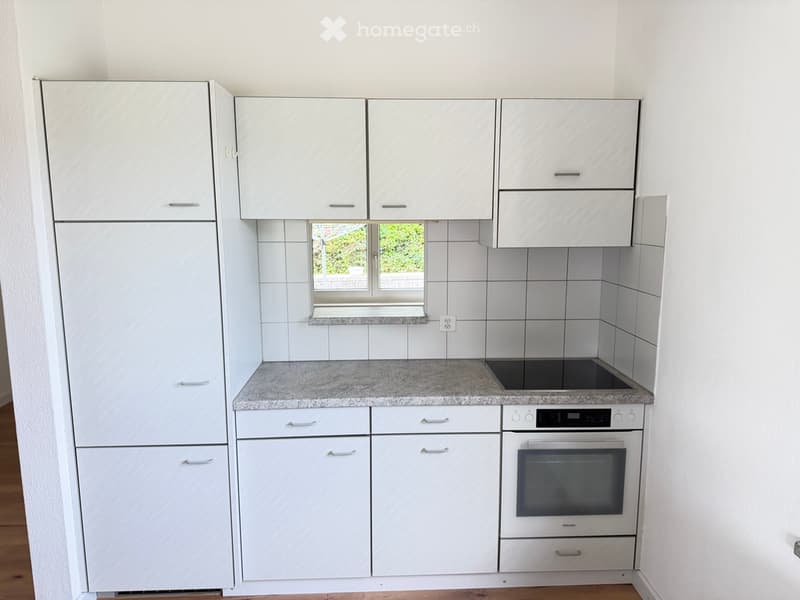 Modern kitchen with white cabinets, granite countertop, built-in oven, refrigerator, and a window offering a view of greenery.