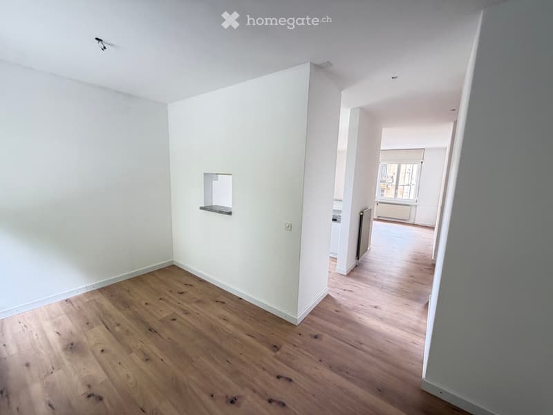 Empty room with light wooden flooring and white walls, featuring a small built-in shelf and a visible electrical outlet.