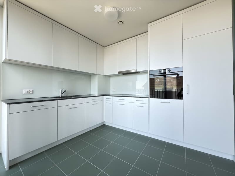 Modern kitchen with white cabinets, dark countertops, and grey tiled flooring. Features a sink with a modern faucet and an integrated oven.