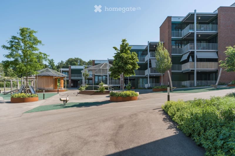 Courtyard area with modern residential buildings, playground equipment, trees, and landscaped greenery.